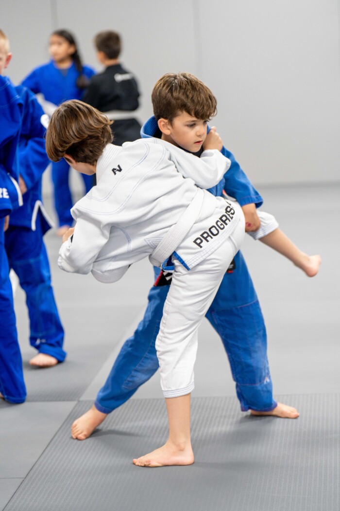 Two young boys grappling, one lifting the other's leg in a takedown attempt