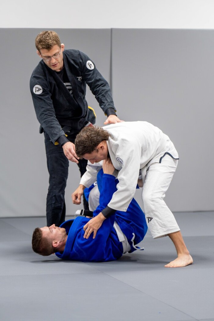 Instructor providing private instruction to two young men grappling each other